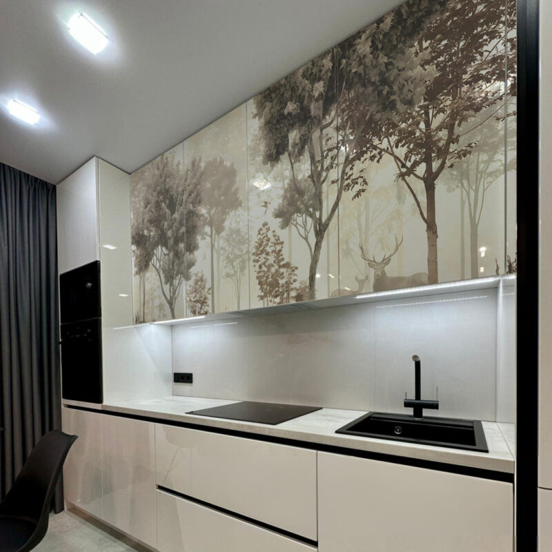 A modern kitchen with white cabinets and a glass backsplash featuring a printed forest scene with deer.