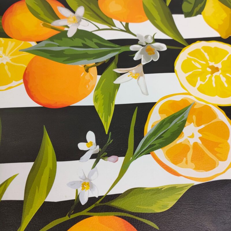 Vibrant pattern of oranges, lemons, leaves, and white flowers on a black and white striped background. this on leather.