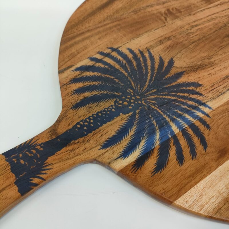 Oval wooden serving board with a black palm tree design and a handle.