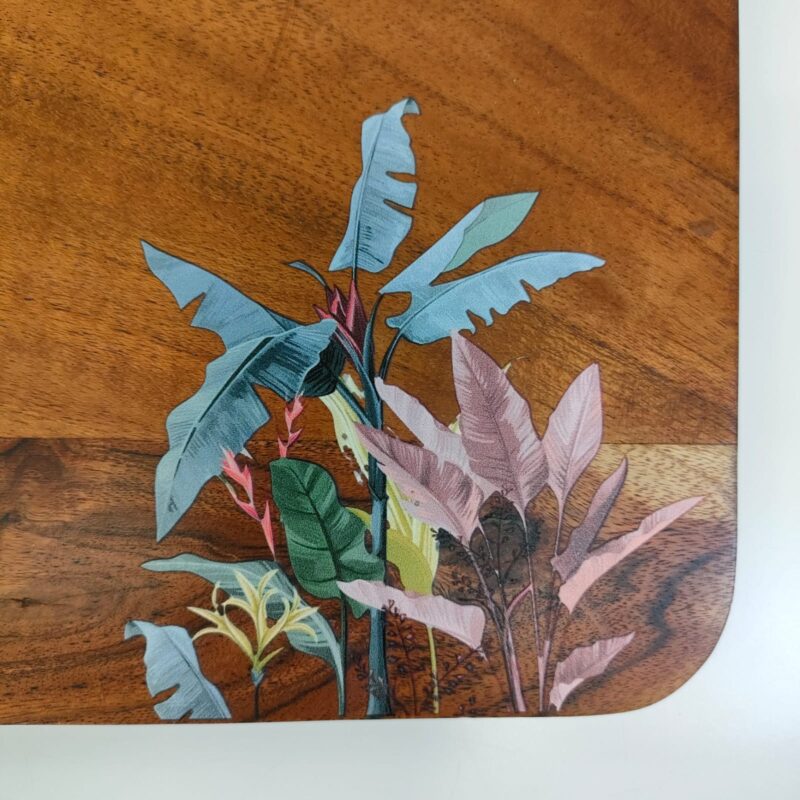 Close-up of a wooden board with UV-printed tropical leaf design in shades of blue, green, and pink