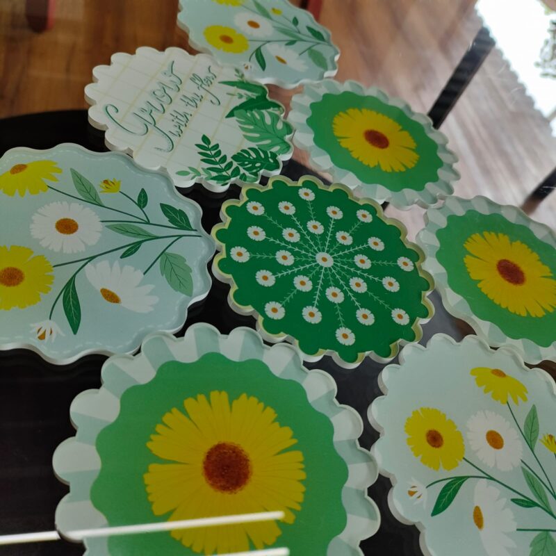 A set of circular acrylic coasters with floral designs and text.